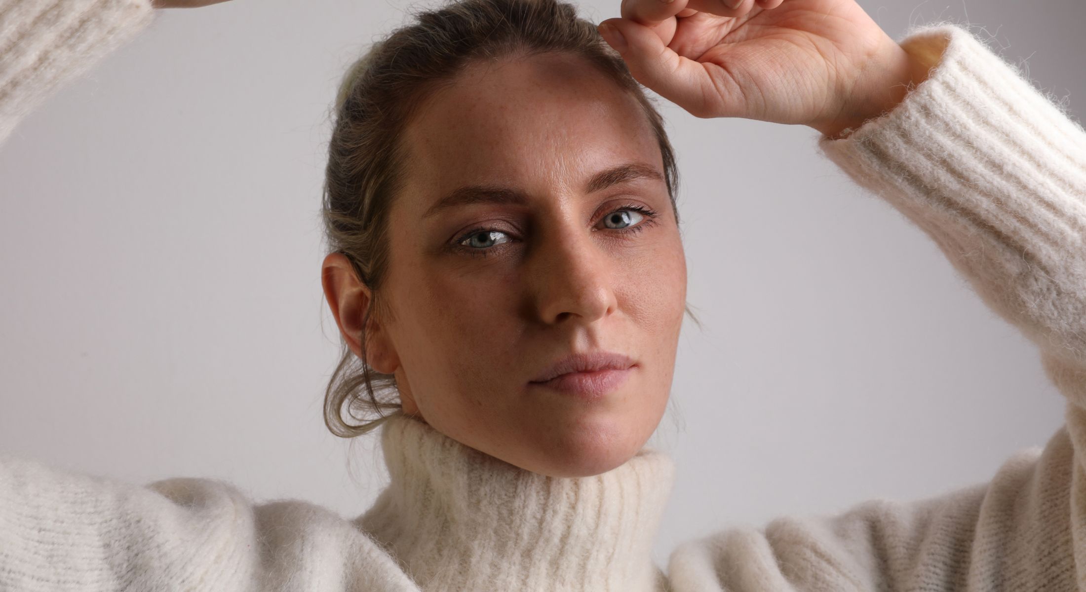 Woman in a cozy sweater against a neutral background.